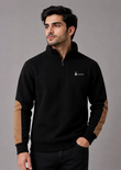 A man wearing a black quarter-zip pullover sweatshirt with tan color-blocked elbow patches and a small white embroidered logo on the left chest, posed against a solid gray studio background.
