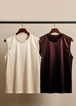 Two sleeveless shirts, one beige and one brown, on hangers against a neutral background.