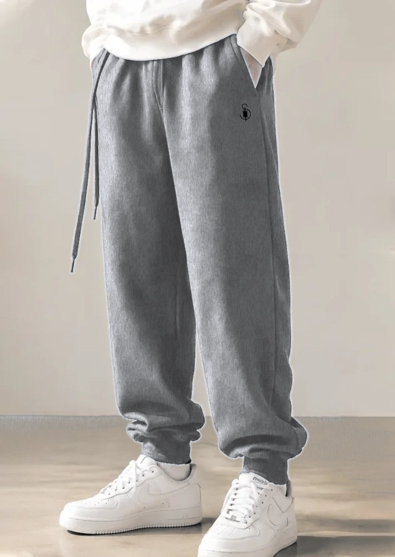 Gray jogger sweatpants with a drawstring waist and elastic cuffs, shown on a model wearing white sneakers against a neutral indoor background.