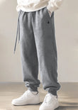 Gray jogger sweatpants with a drawstring waist and elastic cuffs, shown on a model wearing white sneakers against a neutral indoor background.