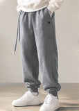 Gray jogger sweatpants with a drawstring waist and elastic cuffs, shown on a model wearing white sneakers against a neutral indoor background.